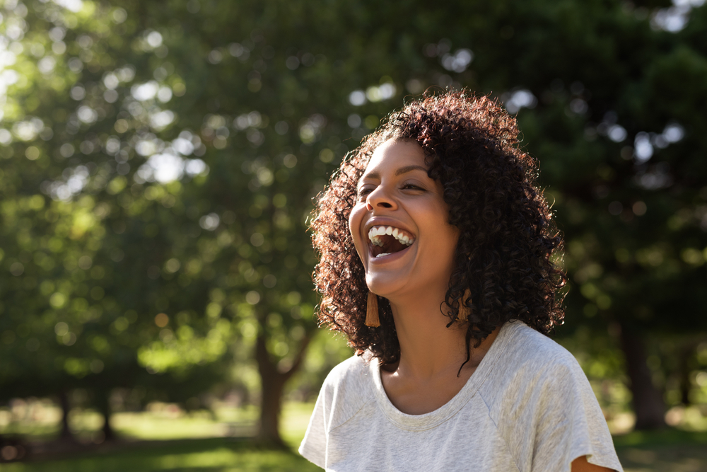 Young,Woman,With,Curly,Hair,Laughing,While,Standing,Outside,In